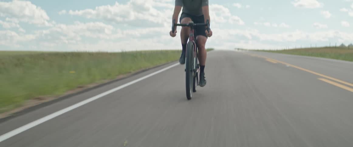 Man wearing a safety helmet riding his bicycle down an empty road during the day