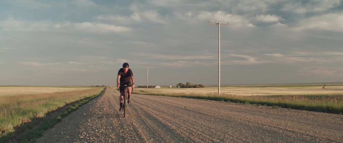 Man wearing a helmet riding a bicycle on a dirt road in a rural area