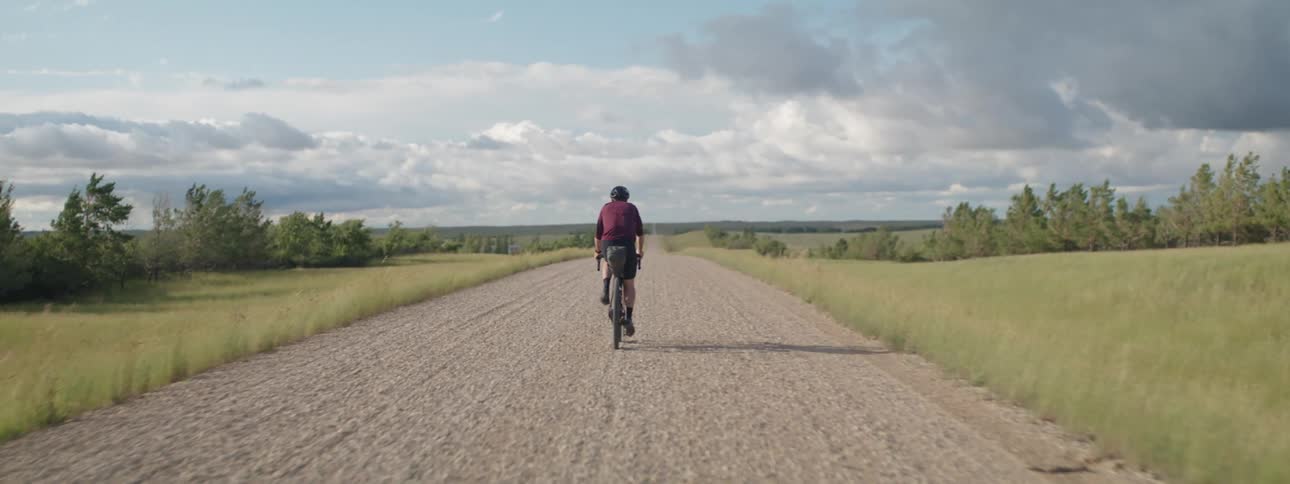 A man is riding a bicycle on a wide open rural dirt road