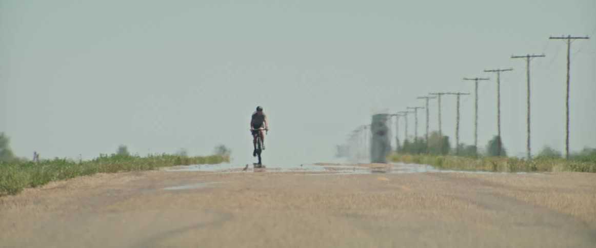 Male cyclist rides bicycle on hot rural road displaying mirage effect
