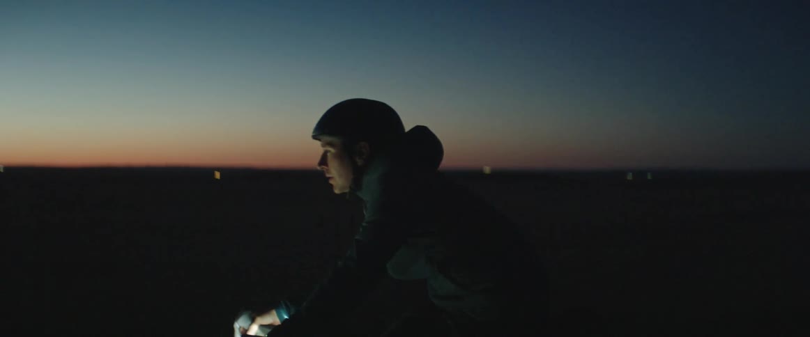 Man with helmet and coat rides bicycle on country road at dusk