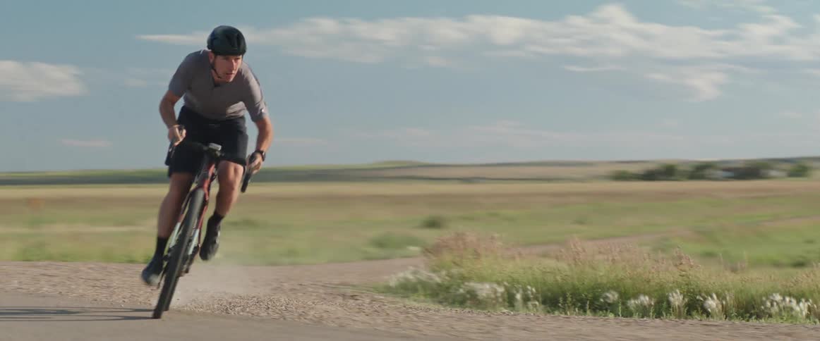 Male cyclist wearing a helmet merges his bike onto a road in a rural area