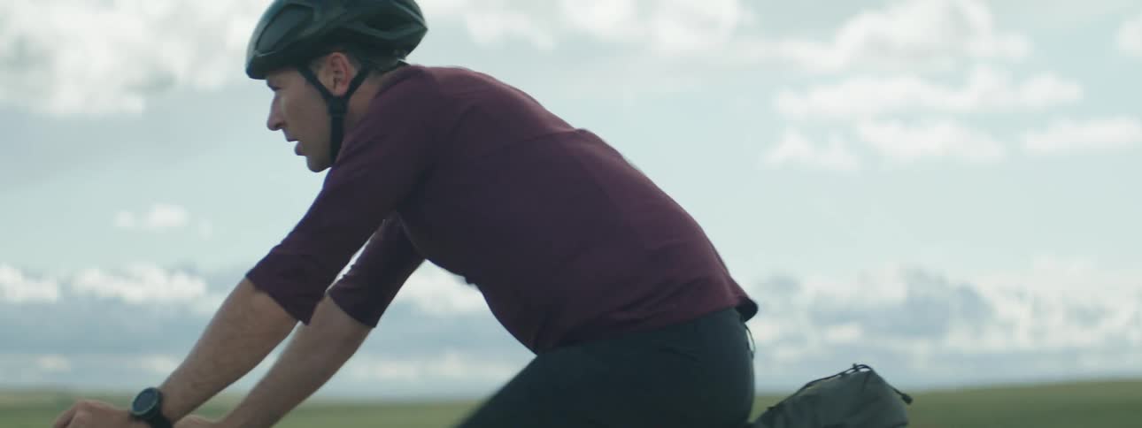 Male cyclist with helmet red sweatshirt and black shorts rides bicycle on road in the countryside