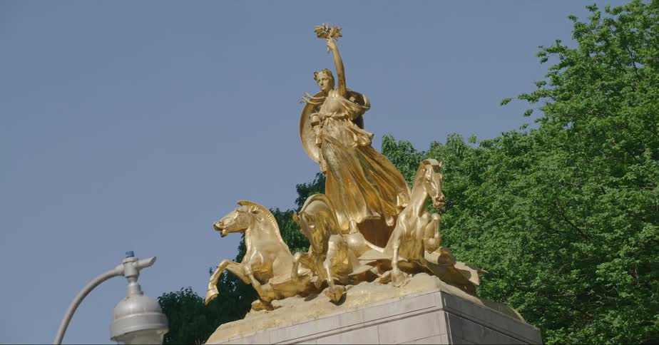 A bird sits on a light pole near a large statue
