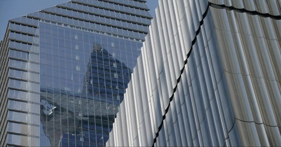 Skyscrapers shiny surface reflects other buildings in downtown under a clear blue sky