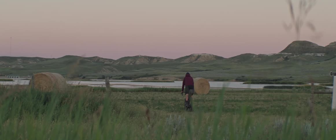 Man rides a bicycle on a field with hay bales in the evening