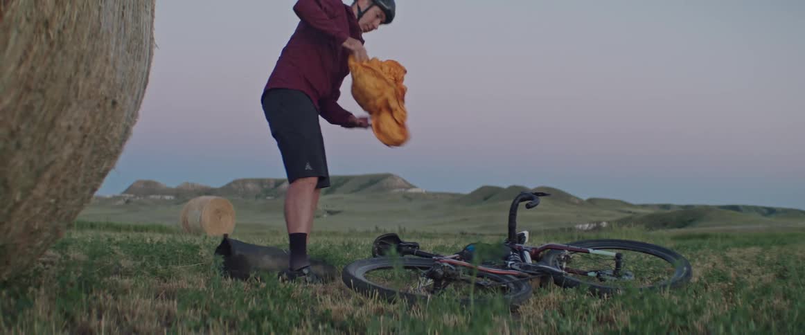 Man unpacking a tent near a bicycle laying in the ground on the countryside