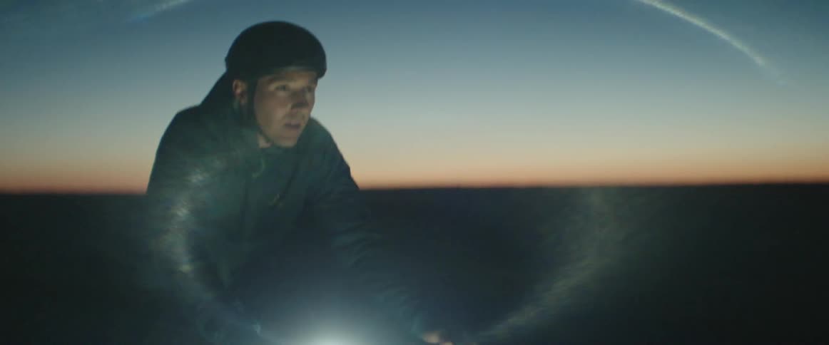 Man wearing a helmet rides a bicycle on a rural road after sunset with the headlight on