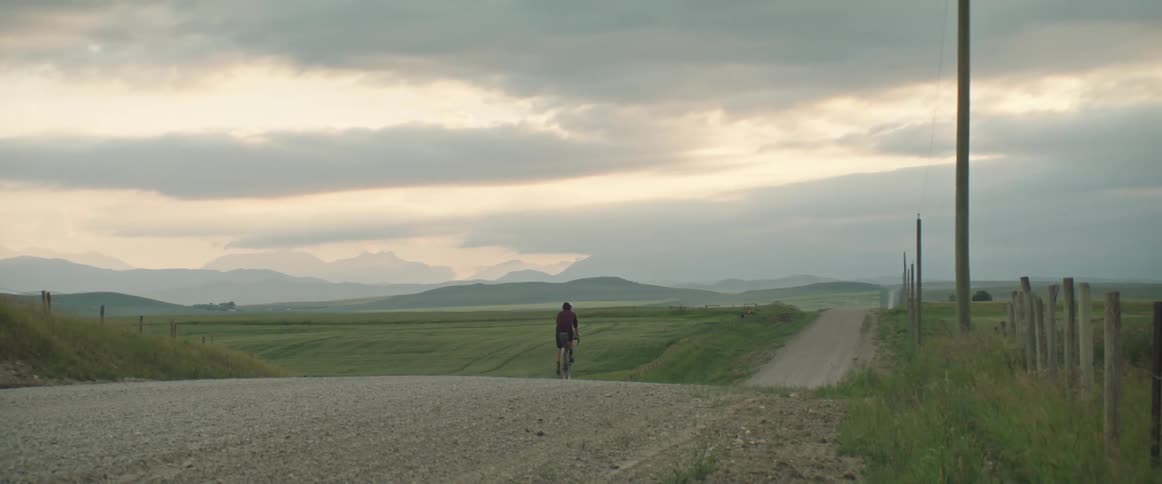 Male cyclist with helmet red sweatshirt and black shorts rides bicycle on country road in countryside at dusk