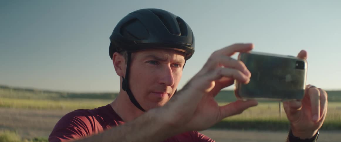 A man in a bicycle helmet takes a photo with his smartphone