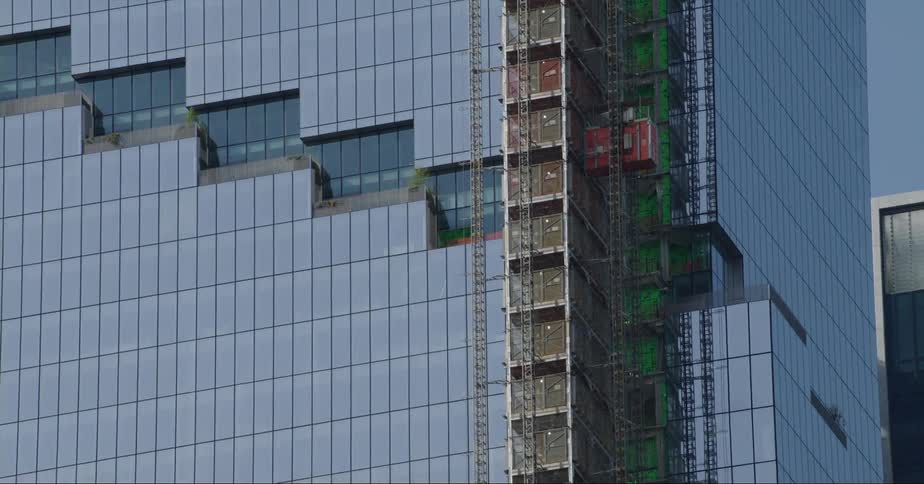 An exterior elevator descends down a tall building with construction scaffolding attached to it