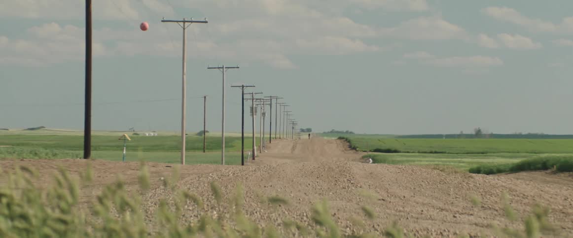 A cyclist is riding a bicycle on a hot rural dirt road lined with utility poles