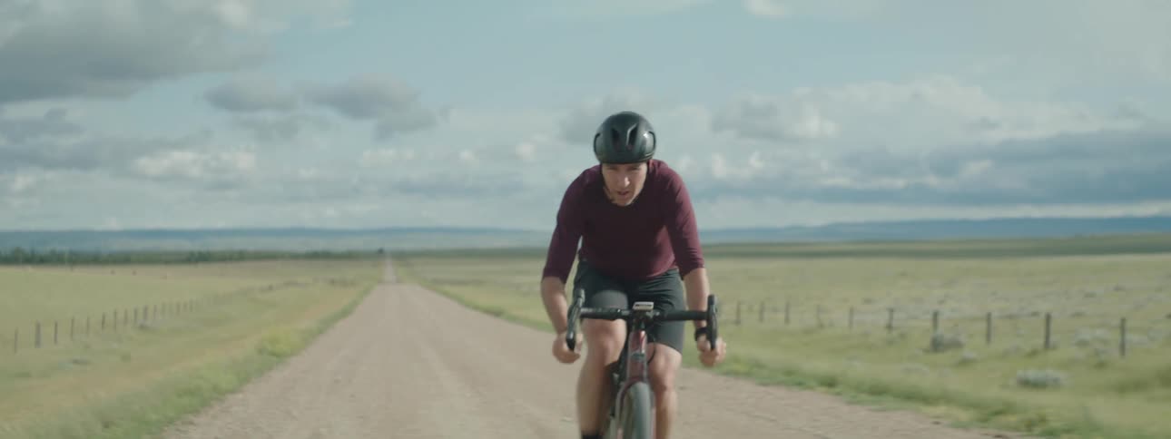 Determined male cyclist rides bicycle on dirt road between fields