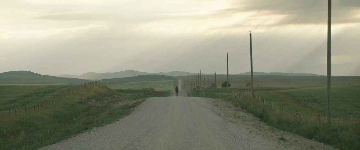 Man wearing a helmet rides a bicycle on a rural road at sunset