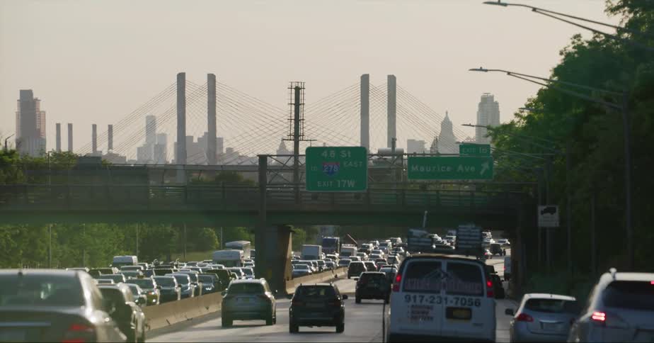 Multiple vehicles travel a large highway under a bridge and near a city
