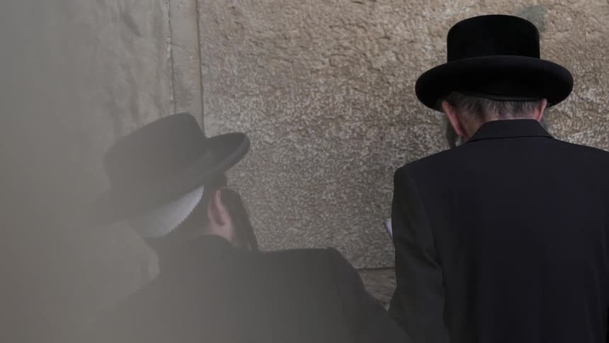 Men in black hats stand next to a stone wall