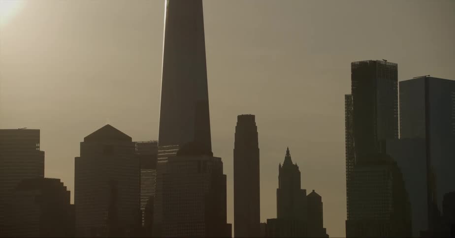 Skyscraper with spire and high rise buildings are silhouetted against the sky in the city
