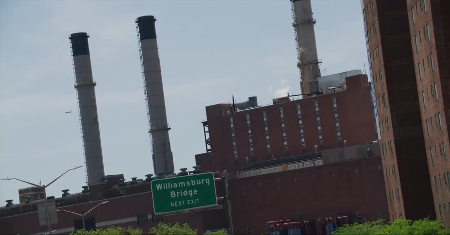 Plane flies past large factory with several chimneys