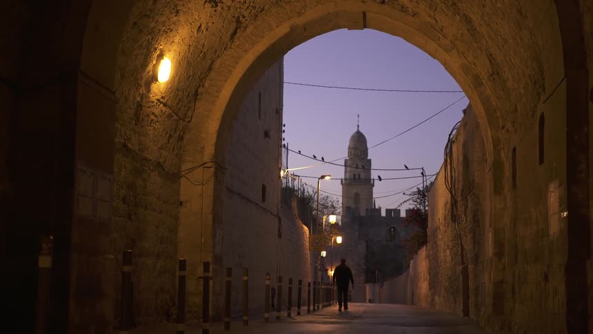 A man walks down a street at dusk