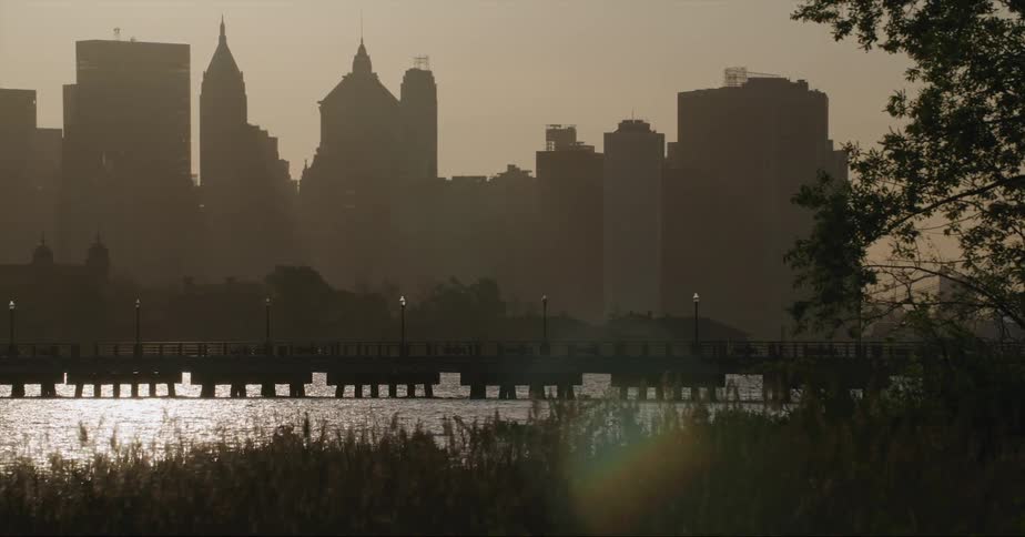 Bridge over a river next to the silhouette of the tall skyscrapers on the city skyline at evening