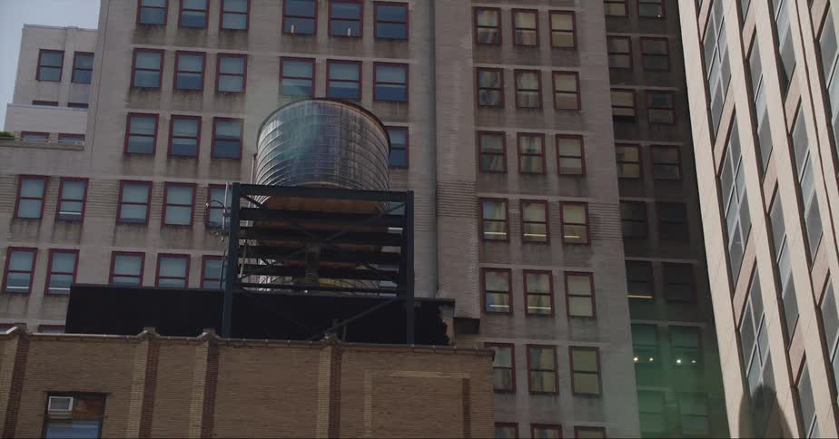 A rooftop water tower on a city building surrounded by high rises on a bright sunny day