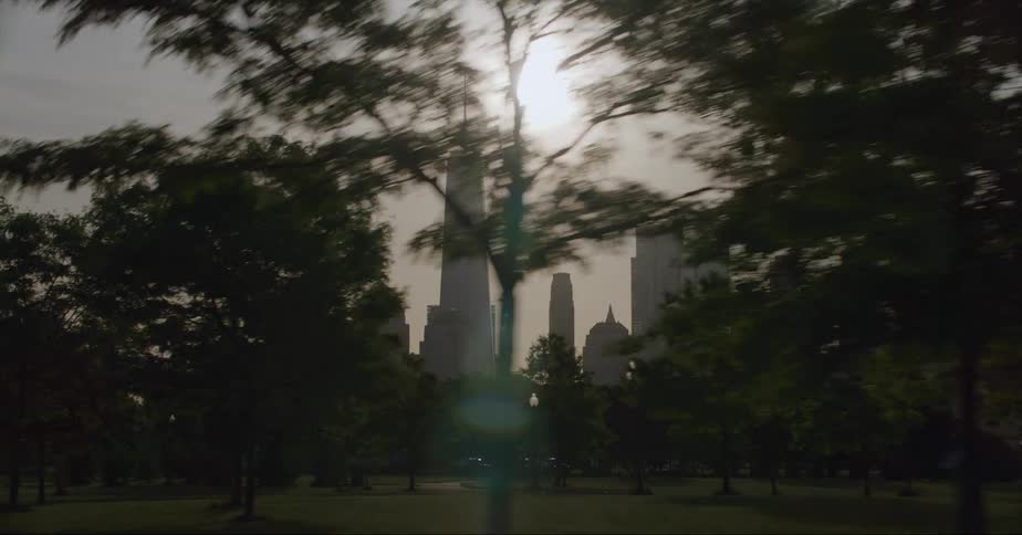 Distant view of skyscraper with spire and high rise buildings are silhouetted against the shining sun in the city
