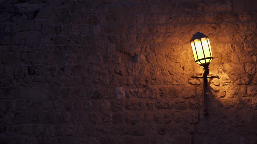 A single lamp is on the side of this stone wall