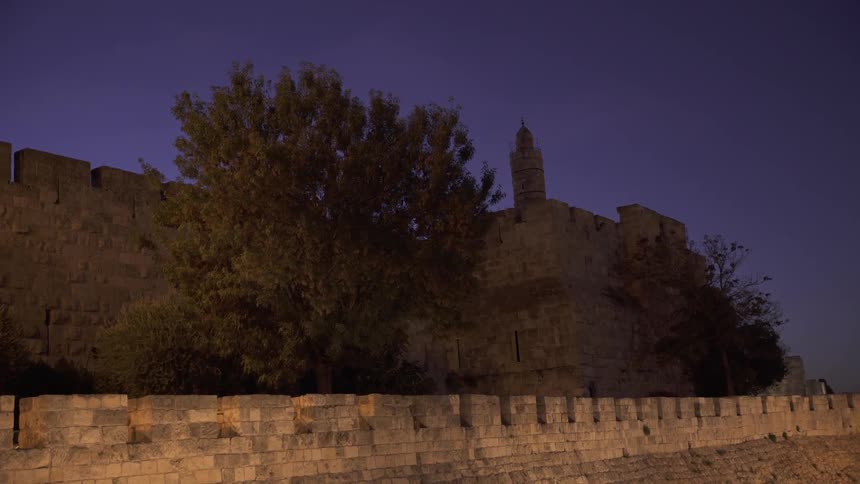 A brick wall leads to a castle behind it at dawn