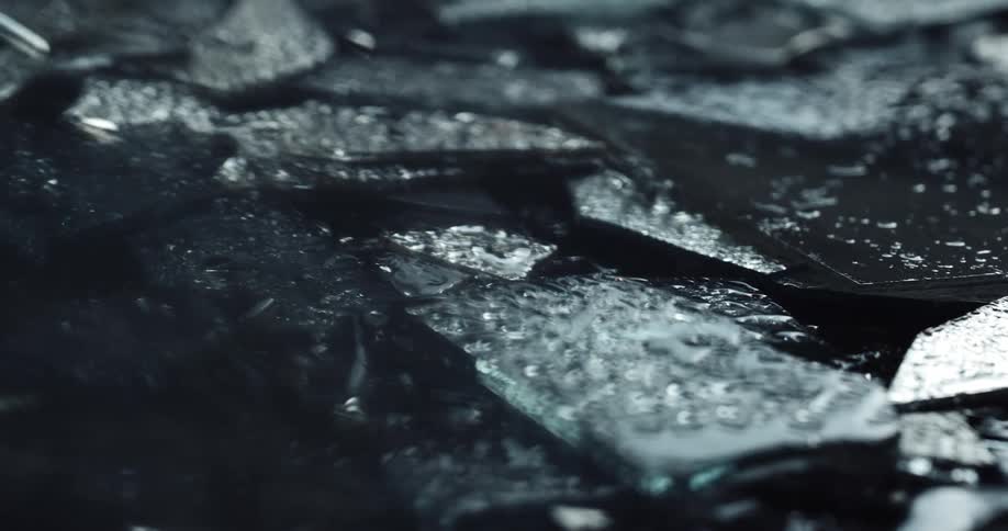 Flashing red and blue lights shine across broken shards of glass as it rains