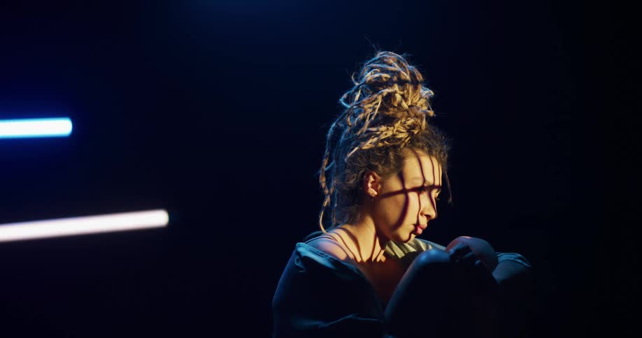 Woman with a chaotic hairdo sitting inside a dimly lit room holding a newborn baby