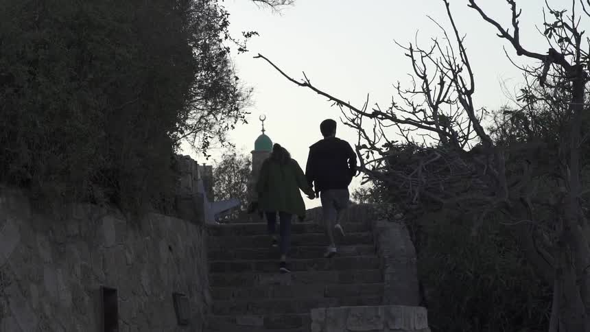 A man and woman hold hands while walking up stone steps