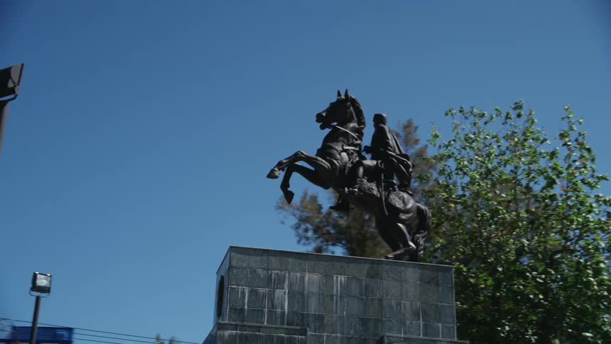Pedestrian walks along avenue past statue of rider and rearing horse
