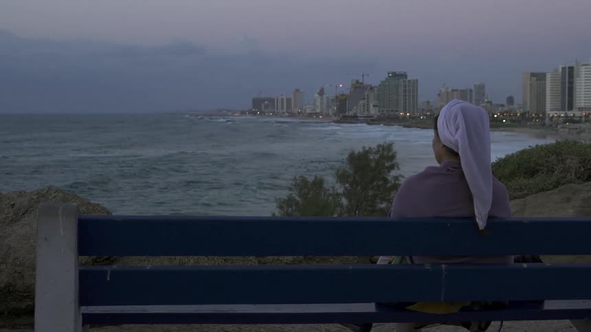A woman sits on a bench near the beach
