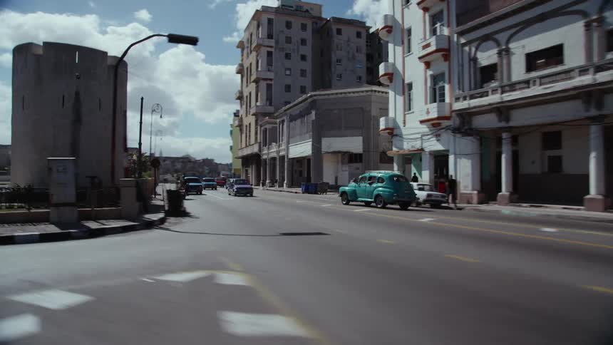 Cars driving down a city street as a few pedestrians walk about