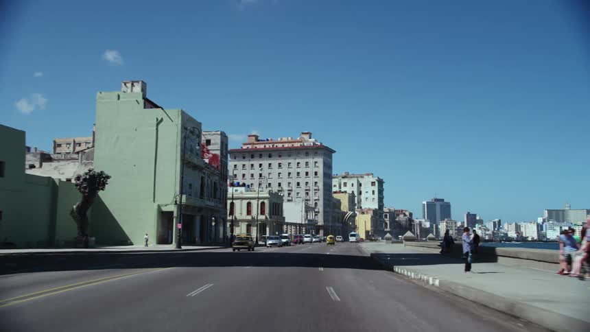 People are walking on a sidewalk towards downtown as traffic moves on the streets and the tall city buildings are in the distance