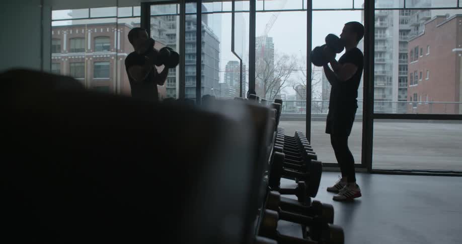 A man faces a mirror as he lifts barbells