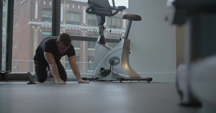 A man is stretching in a gym as someone walks by