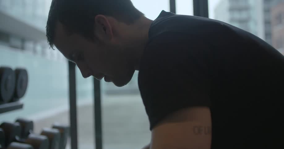 Sweat drips off a man as he sits in a gym during the day