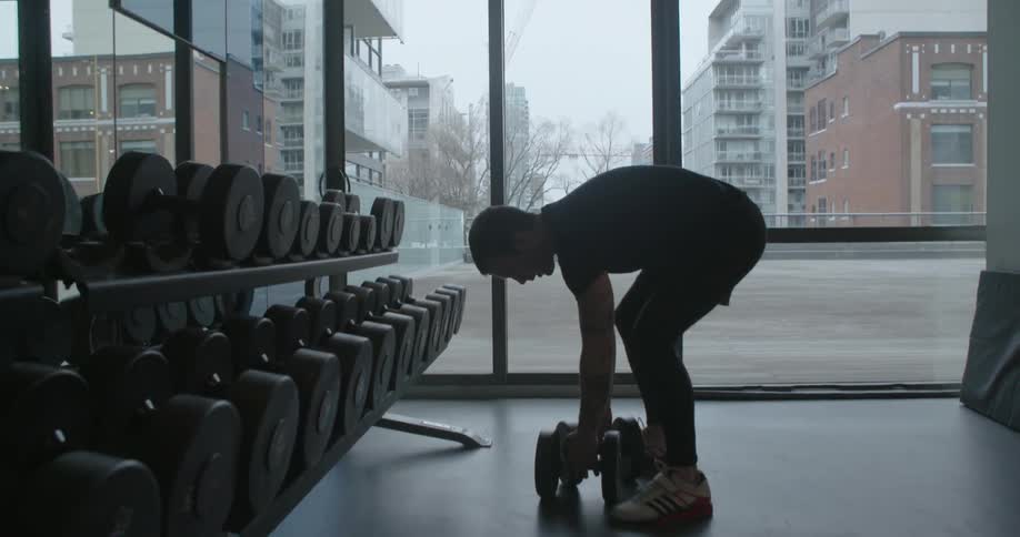 A man bends down to pick up weights in a fitness room