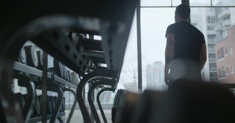 A man working out in a gym stands up from a sitting position and walks over to some weights