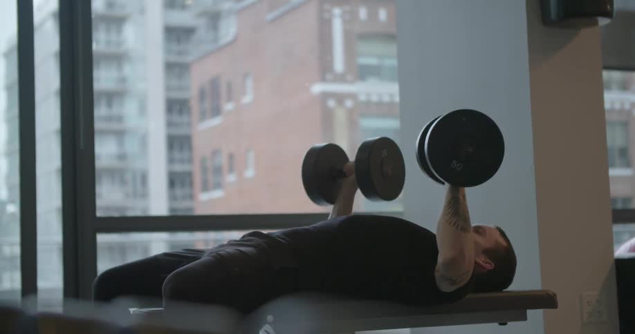 A man is lifting barbells while laying on a bench