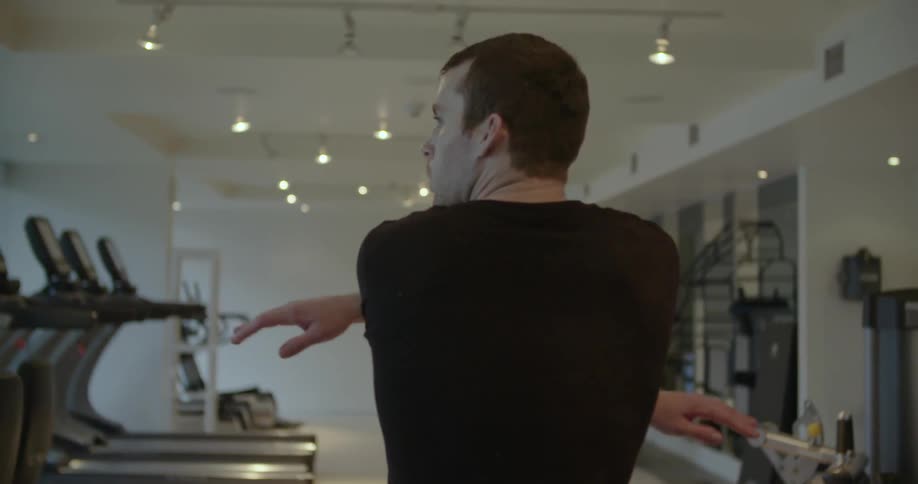 A man is stretching as he walks through a gym