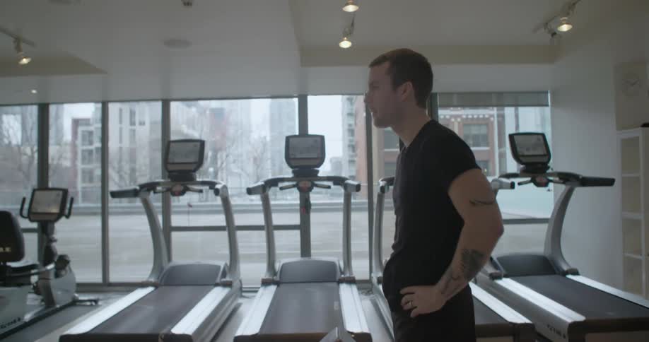 A man breathing heavily next to a row of treadmills