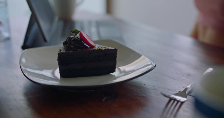 A waitress sets a piece of chocolate cake down on a table for a woman working on her laptop