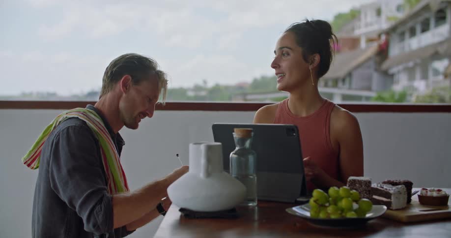 A man points at the computer screen and writes notes as a woman talks during a meeting