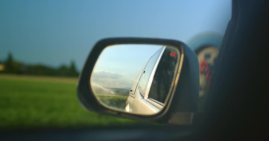 Reflection in a wing mirror as a truck drives past farm equipment in a field