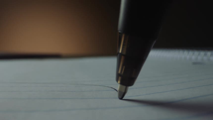 A pen is leaving a waving line of black ink across a sheet of notebook paper