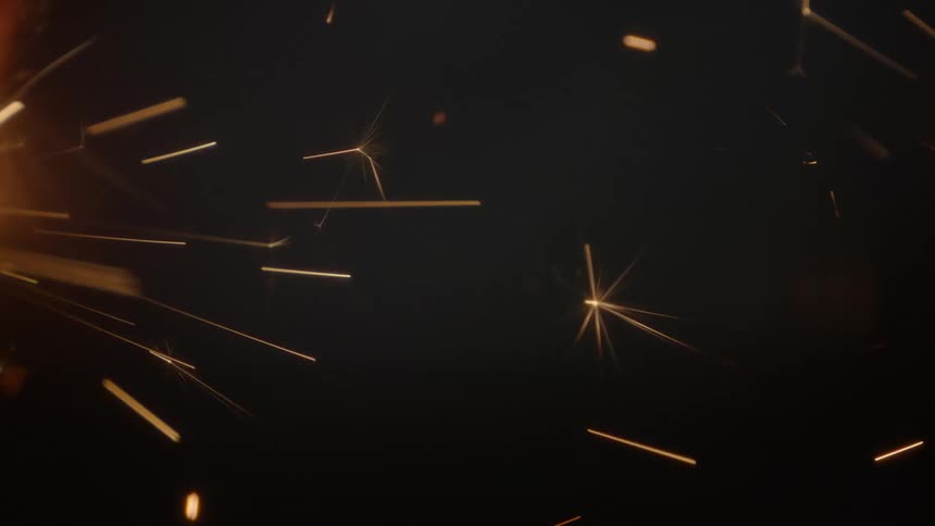 Sparks from a flame fly across the darkness
