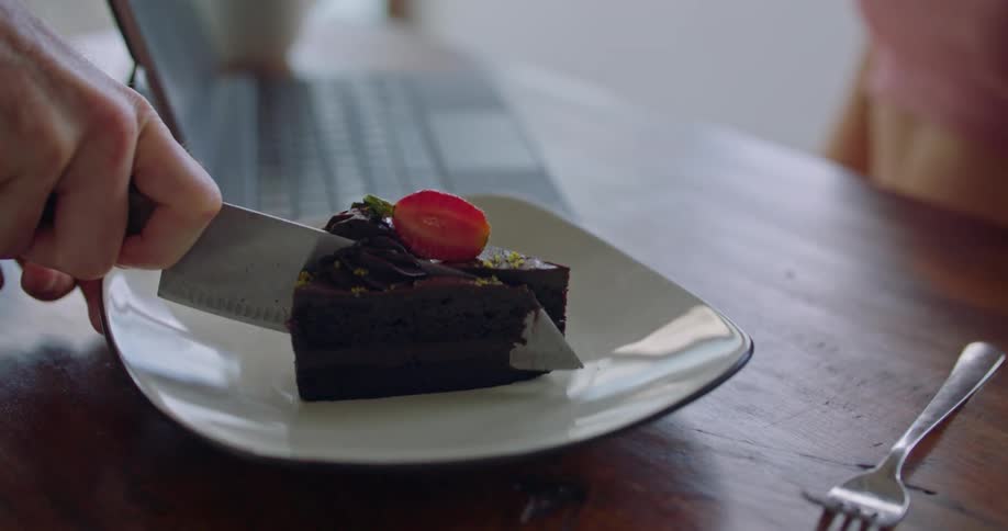 A person slicing a piece of chocolate cake with a sharp knife