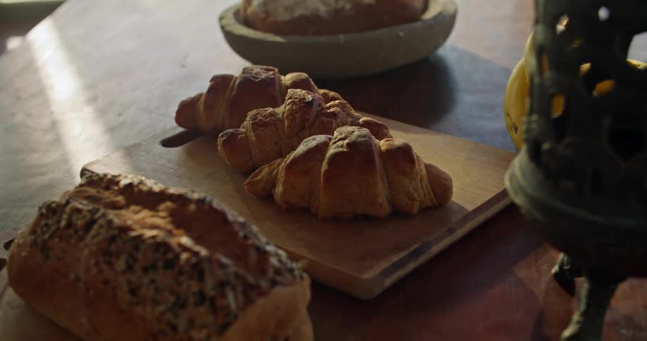 A trio of croissants sit atop a cutting board located on a table along with a loaf of bread